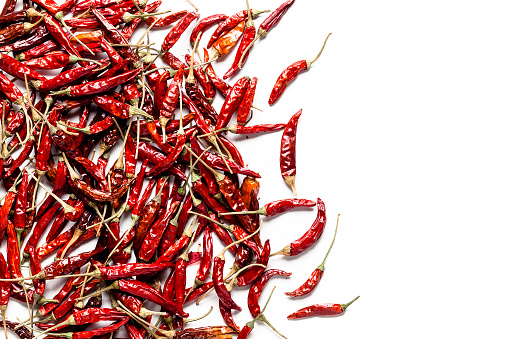 Scattered dried chili peppers coming from the left of an horizontal frame leaving useful copy space for text and/or logo on white background. Predominant colors are red and white. High key DSRL studio photo taken with Canon EOS 5D Mk II and Canon EF 100mm f/2.8L Macro IS USM.