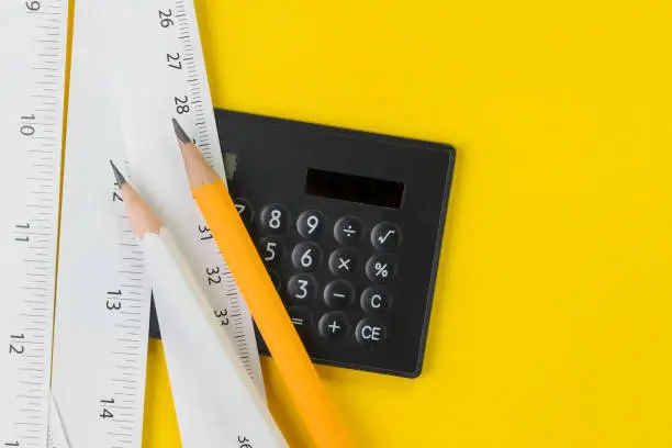 Calculator, pencils and white measuring tapes with centimetre and inches on vivid yellow background, length, long or maker instrument and enginerring tools concept.