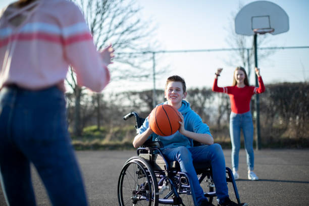 chico adolescente en silla de ruedas jugando baloncesto con amigos - teen activity fotografías e imágenes de stock