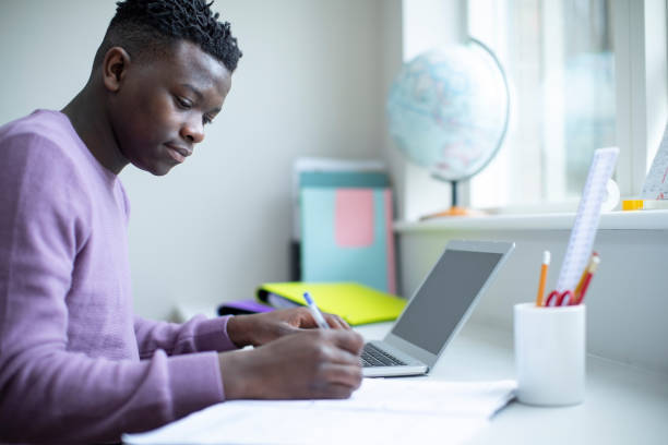 istock Teenage Boy Sitting At Desk Doing Homework Assignment On Laptop 1137349674