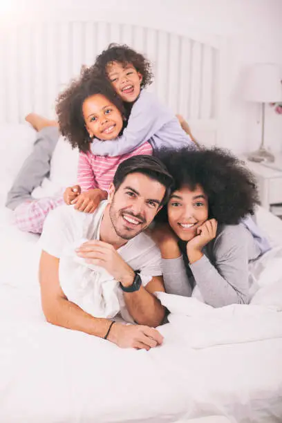 Photo of Happy mixed race family lying on bed and looking at camera