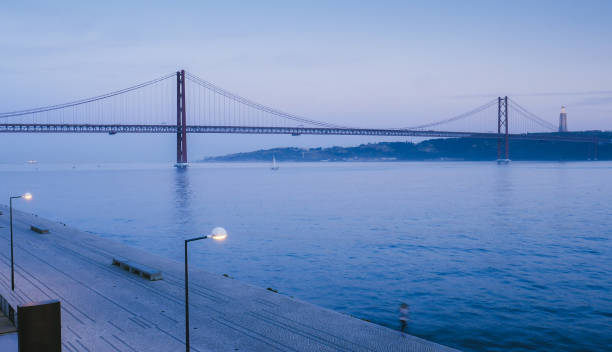 wahrzeichen 25 april brücke auf dem fluss tagus mit cristo rei im hintergrund, lissabon, portugal - blue bridge stock-fotos und bilder