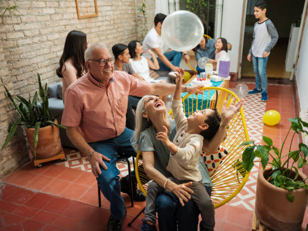 Happy mexican grandparents and grandson playing with balloon Happy mexican parents sitting with their grandson on chairs and playing with a balloon during a birthday celebration at home. reunion stock pictures, royalty-free photos & images
