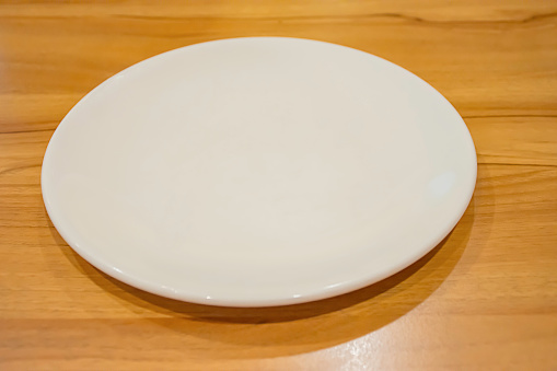 Top view of the white ceramic plate on a wooden table