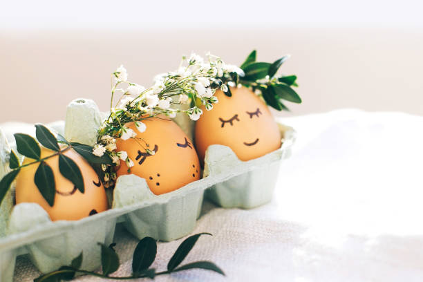 istock Happy Easter,  eco concept. Stylish Easter eggs with cute faces in floral wreath crowns in carton tray on rustic background. Modern easter eggs with flowers and sleepy eyes in sunny light 1137359851