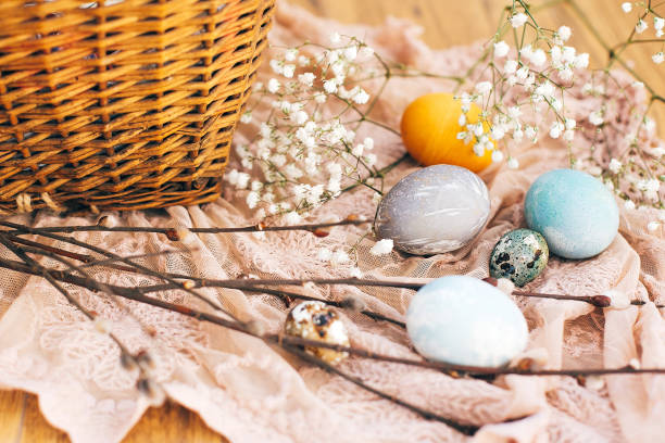 istock Stylish Easter eggs with spring flowers and willow branches on rustic fabric at wicker basket with holiday food in sunny light. Modern easter eggs painted with natural dye. Happy Easter 1137361052