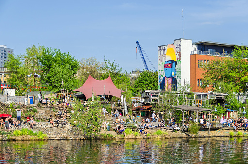 Berlin, Germany - April 22, 2018: Holzmarkt - an urban village made of recycled windows, secondhand bricks and scrap wood, and the alternative cultural complex at the river Spree with people enjoying the warm day