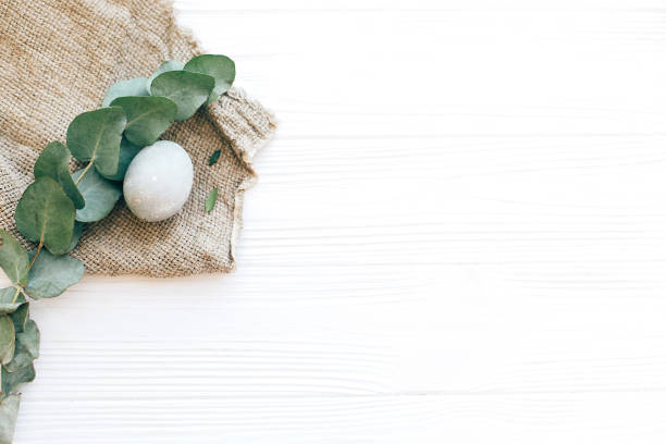 istock Stylish Easter egg on rustic fabric with eucalyptus branch on white wooden background. Modern pastel eggs painted with natural dye. Happy Easter, minimal greeting card mockup. Flat lay 1137364321