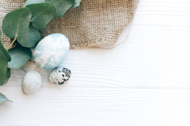 istock Stylish Easter eggs on rustic fabric with eucalyptus branch on white wooden background. Modern pastel eggs painted with natural dye. Happy Easter, greeting card 1137364748