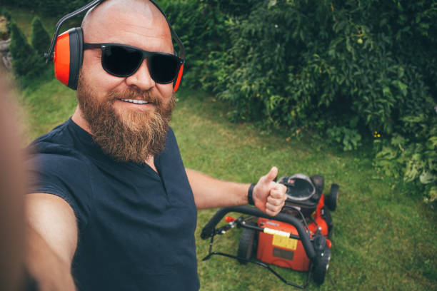 Young bearded man making selfie while mows the lawn, cutting down the grass in the garden stock photo