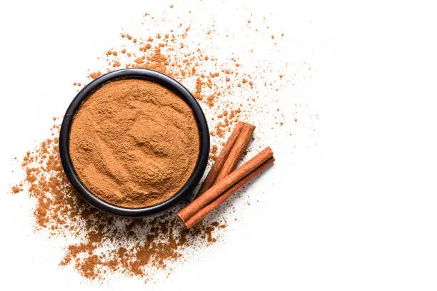 Photo of Spices: cinnamon powder with cinnamon sticks shot from above on white background