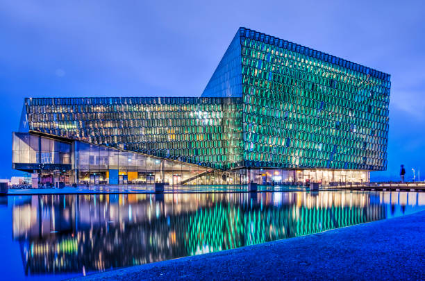 Reykjavik, Iceland, February 26, 2019: Harpa concert hall with illuminated facade reflecting in a pond during the blue hour on a winter evening