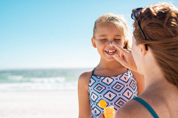 Mother applying suntan lotion on daughter face Young mother applying protective sunscreen on daughter nose at beach. Woman hand putting sun lotion on child face. Cute little girl with sunblock at seaside with copy space. one kid only stock pictures, royalty-free photos & images