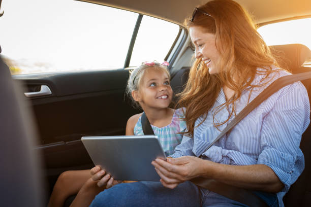 Mother and daughter using digital tablet in car Portrait of smiling mother and happy little girl using digital tablet together in car. Mature woman showing videos to daughter in digital tablet while sitting in a taxi. Cute child learning new things with mother from computer. back seat photos stock pictures, royalty-free photos & images