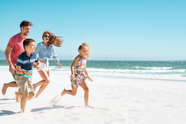 Happy family running on beach Cheerful young family running on the beach with copy space. Happy mother and smiling father with two children, son and daughter, having fun during summer holiday. Playful casual family enjoying playing at beach during vacaton. beach holiday stock pictures, royalty-free photos & images