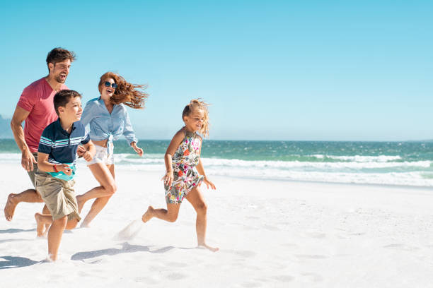 Happy family running on beach Cheerful young family running on the beach with copy space. Happy mother and smiling father with two children, son and daughter, having fun during summer holiday. Playful casual family enjoying playing at beach during vacaton. travel9 stock pictures, royalty-free photos & images