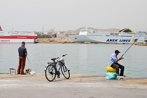Athens, Greece - May 11, 2016: Two male anglers fishing at Piraeus port. Piraeus is the largest passenger port in Europe and the second largest in the World.