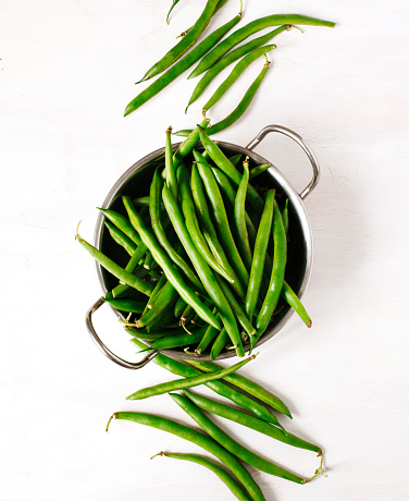 Green beans in bowl on white wooden background, top view.