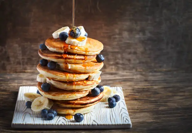 Pancakes with banana, blueberry and maple syrup for a breakfast, wooden background, copy space