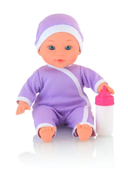 Photo of Baby doll wearing bodysuit and cap, with bottle of milk isolated on white background with shadow reflection. Caucasian new-born child toy wearing violet clothes for newborns. Infant cuddly toy doll.