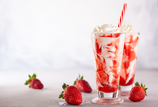 Strawberry milkshake with whipped cream and berry syrup in the tall glass on light background.
