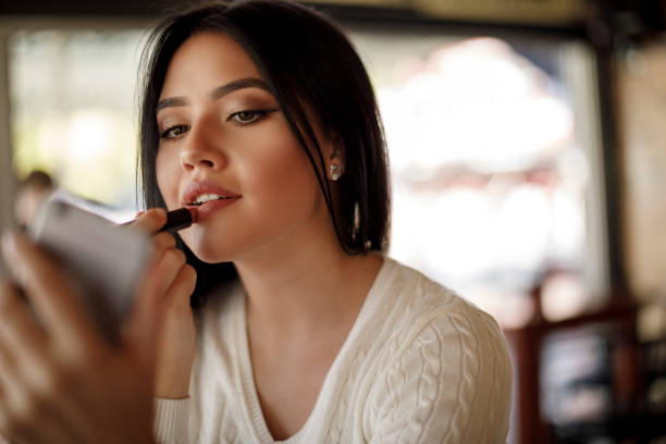 young woman applying lipstick at a cafe - lipstick imagens e fotografias de stock