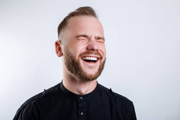 Laughing man with closed eyes, close up studio portrait on gray background