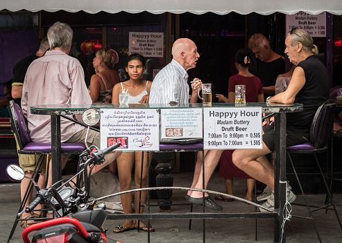 Phnom Penh, Cambodia - January 12, 2019: an unhappy-looking woman in bikini stands near a happy hour announcement (with misspelled 