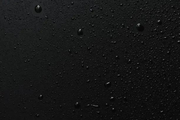 Close-up of raindrops on black rough surface, dark background
