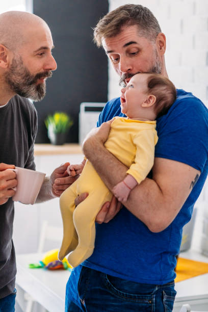 LGBTQ Family - Gay Dads At Home Gay dads with their adopted baby at home. Having fun with their baby. gay dinner table stock pictures, royalty-free photos & images