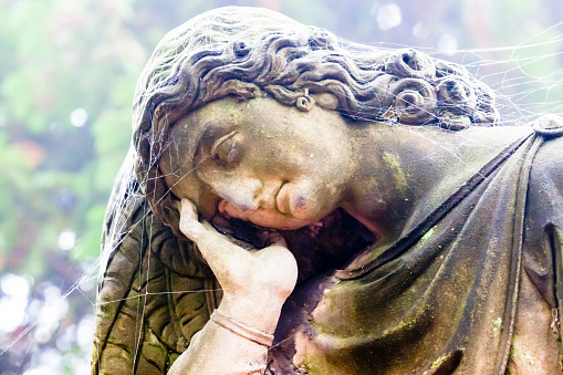 Old statue with spiderweb of sleeping angel in cemetery build in 1850 Czech Republic, background with copy space, full frame horizontal composition