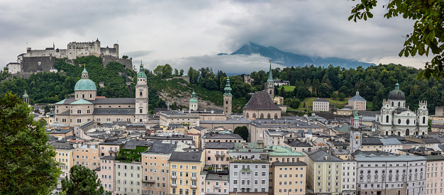 Salzburg City View Façade and Hohensalzburg medieval Castle with cloudy Alps Background and green Forest Hills