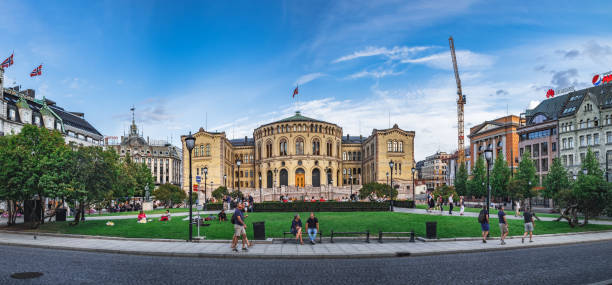 Oslo, Norway - August 3, 2018: People walk and relax in the park next to the building of the Norwegian parliament Stortinget at sunset, Oslo