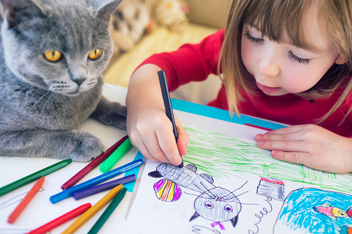 Cute child drawing at home. Kitty next to him.