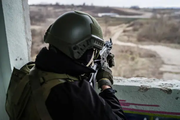 Young Special forces SWAT soldier aiming with assault rifle gun at the ruined building war terrorist battle zone airsoft