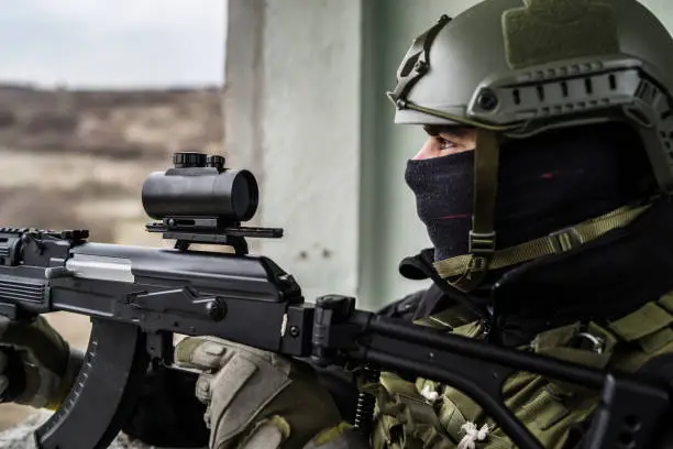 Photo of Young Special forces SWAT soldier aiming with assault rifle gun at the ruined building war terrorist battle zone airsoft