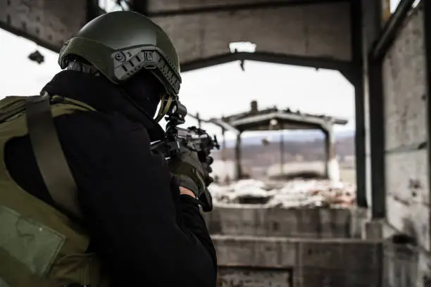 Photo of Young Special forces SWAT soldier aiming with assault rifle gun at the ruined building war terrorist battle zone airsoft