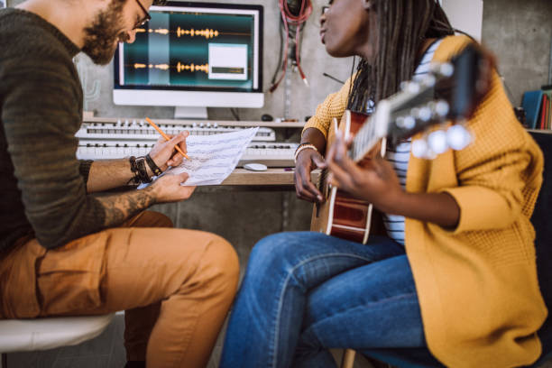 Creative couple writing song in studio Woman playing acoustic guitar, man writing notes on paper in music studio composer stock pictures, royalty-free photos & images