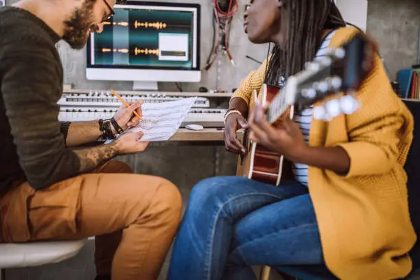 Woman playing acoustic guitar, man writing notes on paper in music studio