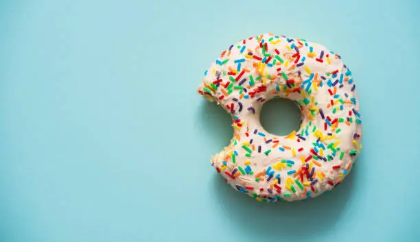 One bite missing of donut on blue background.