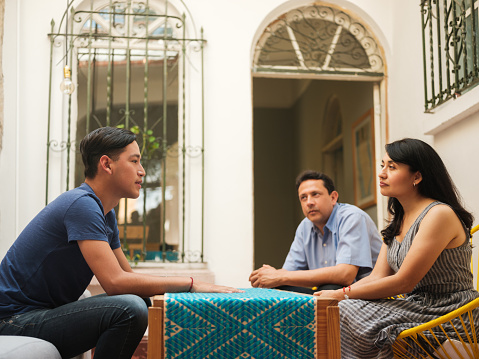 A Mexican father and mother facing their teenage son having a serious conversation.
