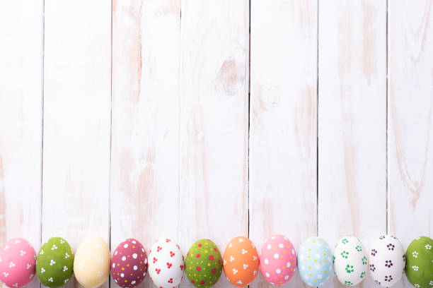 Happy easter! Row Easter eggs with colorful paper flowers on white wooden background.