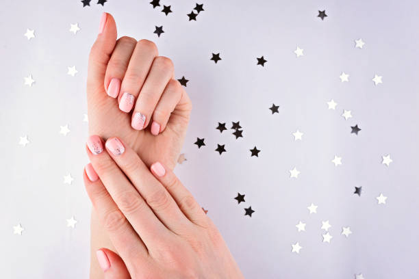 Woman's hands with a pink manicure on a white background with silver stars. Confetti. stock photo