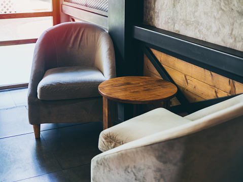 Vintage fabric armchair with round wooden table near the wall, concrete, black steel and wooden wall in cafe.