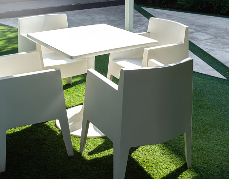 White modern garden dining table and four chairs on green yard. White clean plastic resin outdoor furniture.