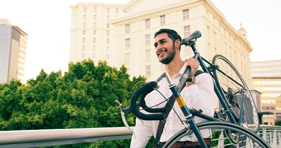 Shot of a handsome young businessman carrying his bicycle on his shoulder while walking through the city