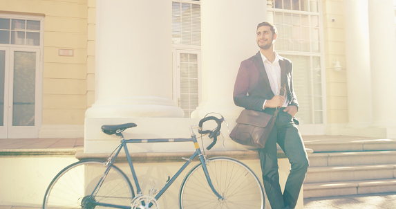 Shot of a handsome young businessman posing next to a bicycle in the city