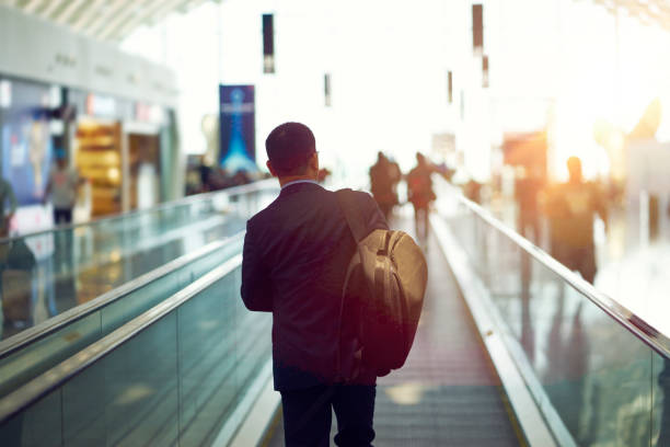 vista posteriore dell'uomo d'affari asiatico che cammina sulla scala mobile dell'aeroporto al tramonto - travel people traveling business travel vacations foto e immagini stock