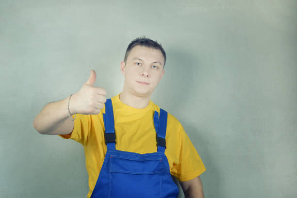 A man in work clothes against a gray wall. Worker shows gesture cool. Photo with space for text.