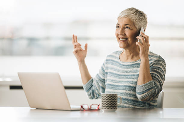 istock Happy mature woman talking on the phone while using laptop at home. 1137507395